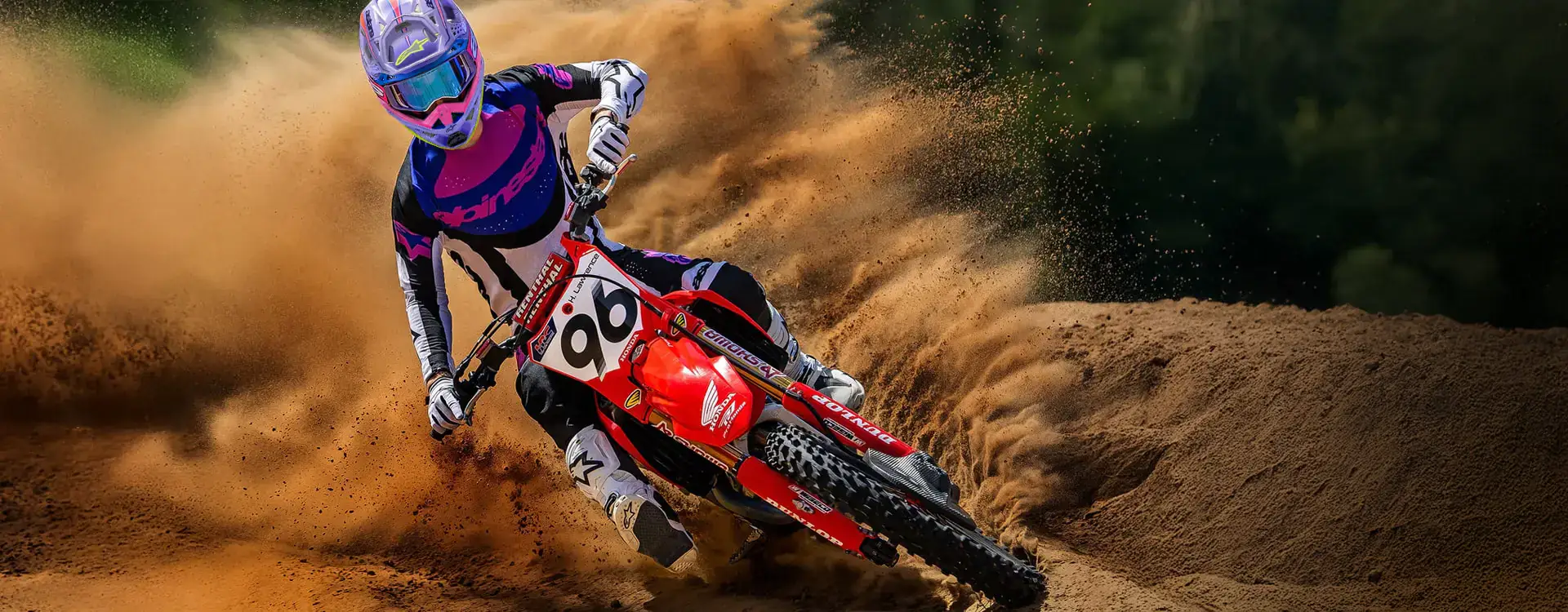 Motocross rider throwing sand through a berm on a red Honda