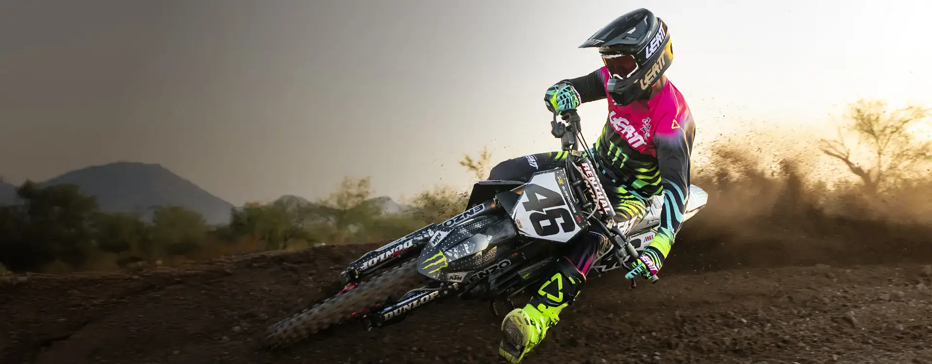 Motocross rider cornering on a dirt track at sunset